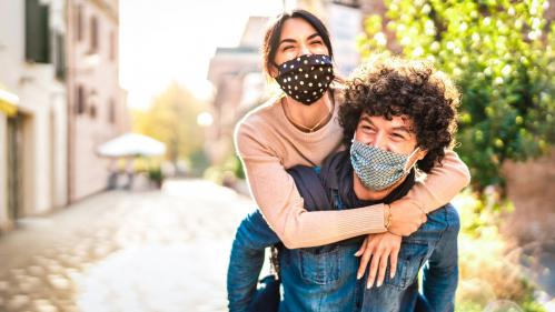 A young man carrying a young woman while outside, wearing masks