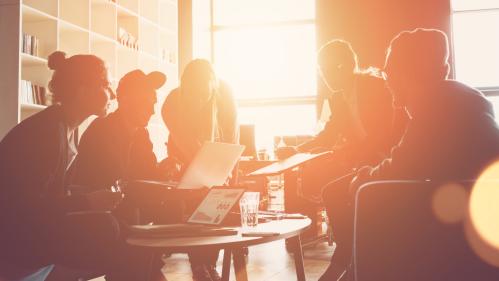 Silhouette of startup business team meeting on the couch in a big open space office. Five people. Intentional sun glare and lens flares. Wide screen, panoramic