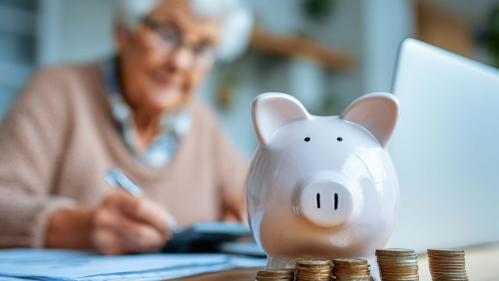 Elderly woman working on paperwork with piggy bank in forefront