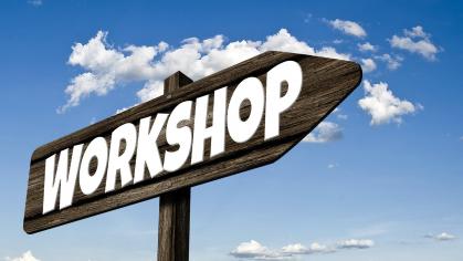 Directional sign with "Workshop" written across it against blue sky with clouds