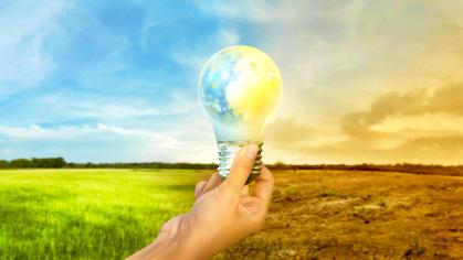 Hand holding a lightbulb in the shape of the Earth in an open field