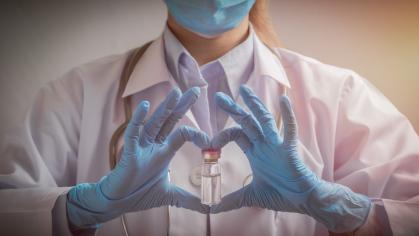 Woman in white lab coat in blue gloves holding vaccine vial