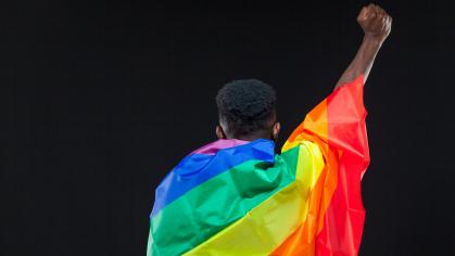 A man holding up his hand in a fist while draped in the Pride flag
