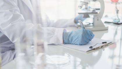 A scientist hands writing on a clipboard in laboratory with test tube microscope and solutions
