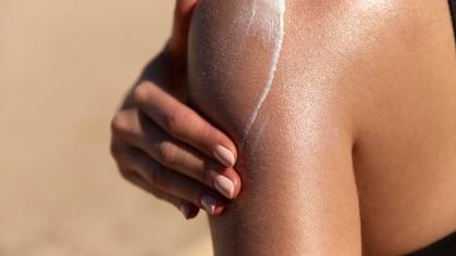 Young woman applying sun cream or sunscreen on her tanned shoulder to protect her skin from the sun. 