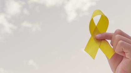 Hands holding yellow gold ribbon over grey sky for childhood cancer awareness