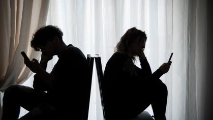 Teenagers sitting back-to-back looking at their cell phones