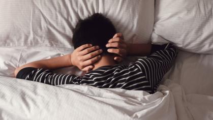 Male covering ears with his hands in bed