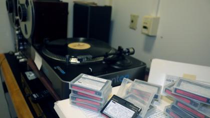 Documented tapes, records, record player on desk in dark room.