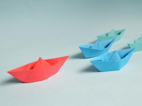 Five paper boats with one red one in the lead