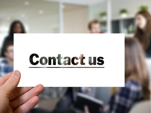 blurred people in background with a hand holding a white card with "Contact us" on it