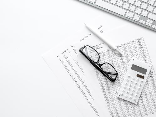 Glasses, calculator, notes and a keyboard on a table