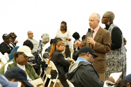 Dr. Gluck speaking into a microphone to a room of mostly seated adults