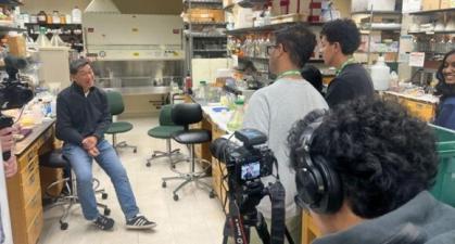 Photo of students interviewing seated Distinguished Professor Eric Lam seated on a stool in his lab