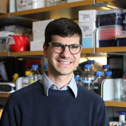 man wearing dark blue sweater with light blue shirt underneath against a lab background