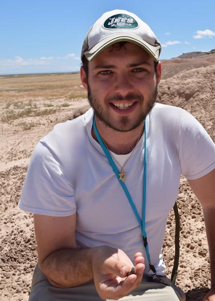 Man with white cap and grey shirt is holding a fossil.
